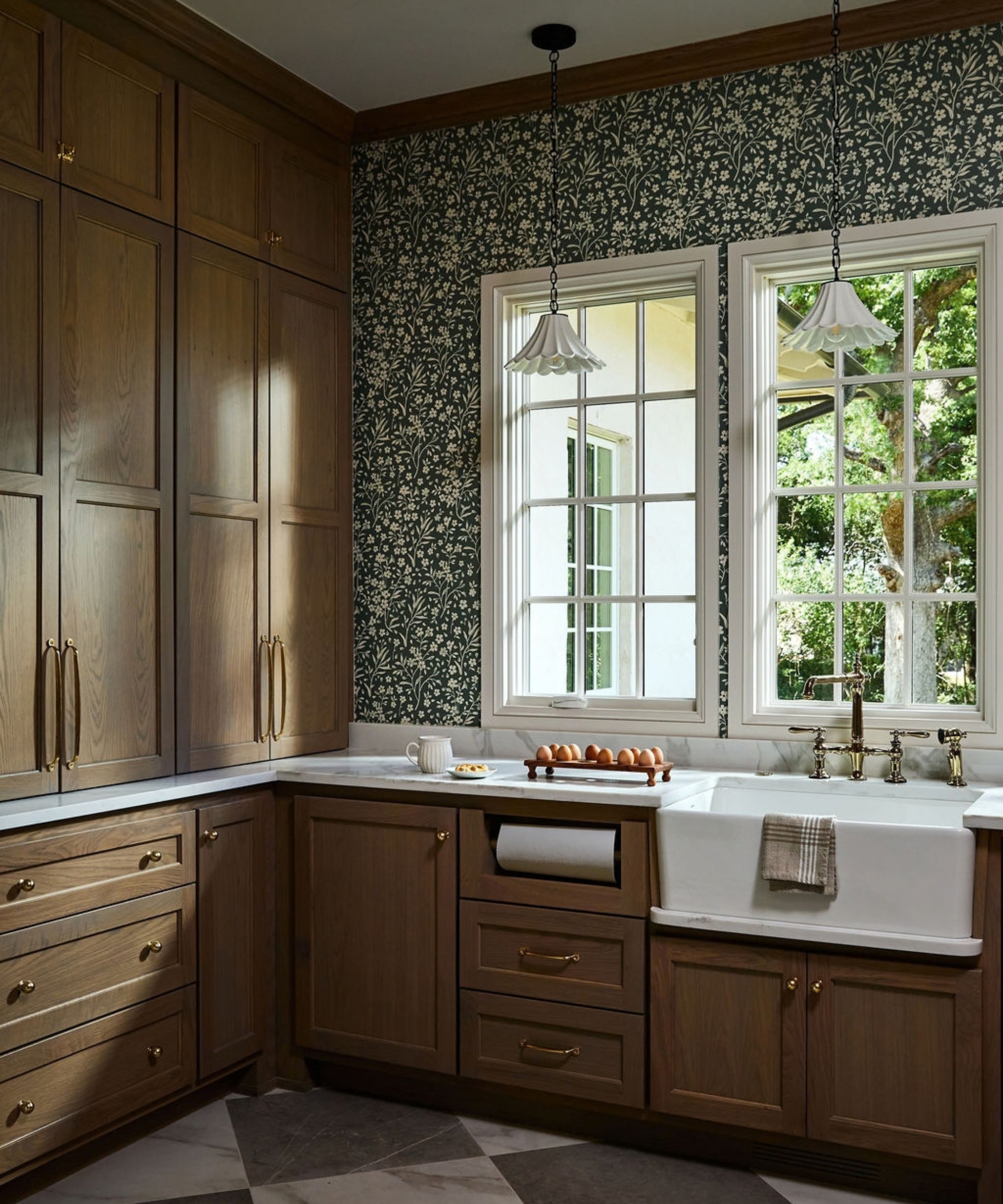 A large back kitchen pantry with wooden cabinets, marble countertops, and a micro floral wallpaper on the walls