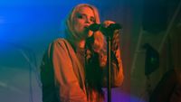 Sky Ferreira holding a microphone on stage with red light on her and blue lights on the background
