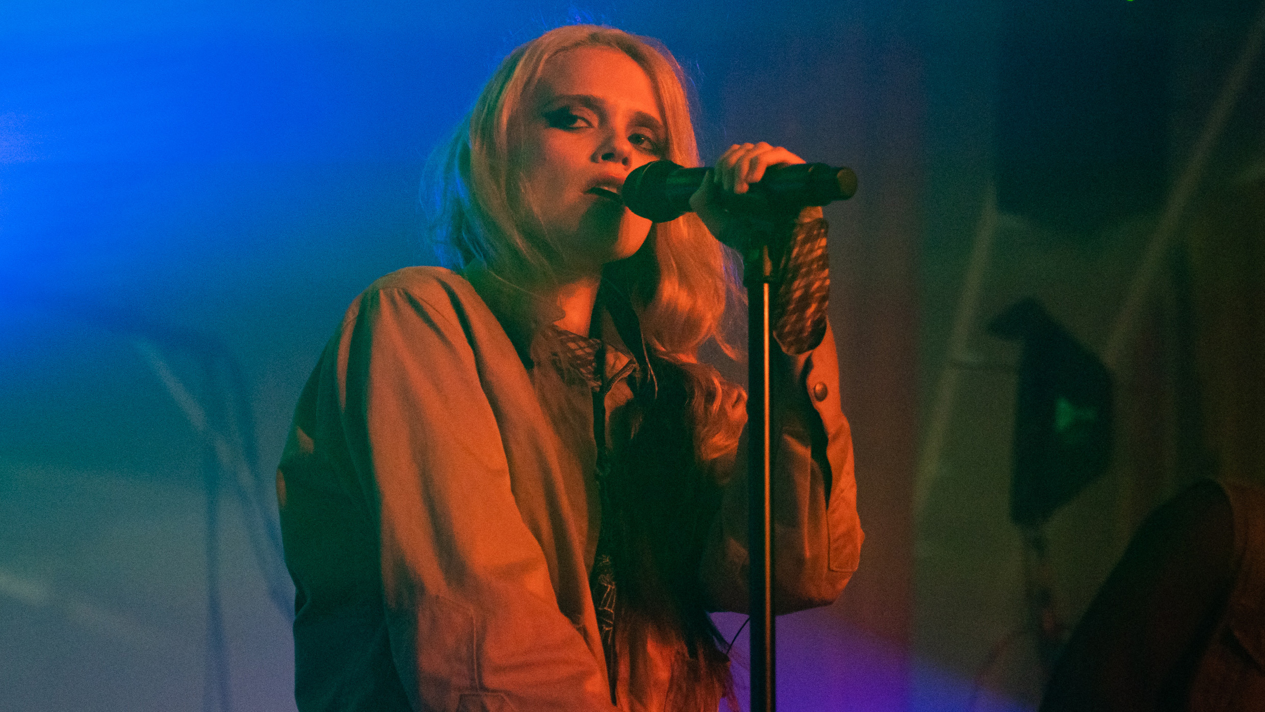 Sky Ferreira holding a microphone on stage with red light on her and blue lights on the background