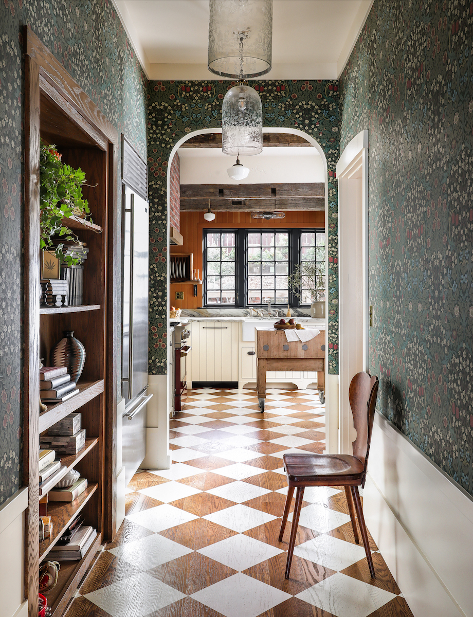 A view into the kitchen down a long hallway toward an arched doorway, with painted wood floors in a checkerboard pattern.