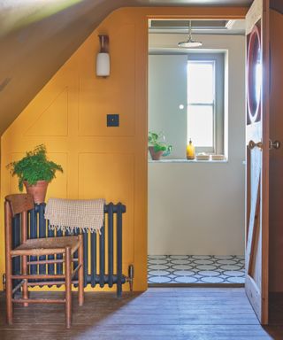 landing with wooden floorboards, chair, charcoal grey radiator, yellow painted panelling, view of bathroom, circle blue tiles, window