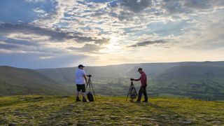 Two men in a landscape framing up their cameras on tripods