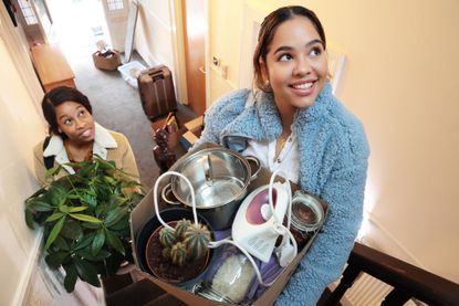two women moving in to apartment carrying box of possessions and household objects upstairs