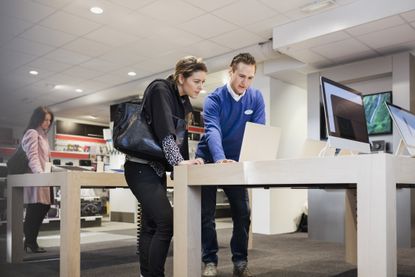 Salesman assisting female customer in buying laptop at store 