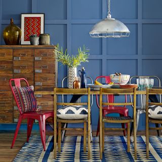 Blue dining room with wallpanelling, patterned rug and mixture of chairs