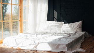 Mattress with white sheets is placed directly on the floor against an open window