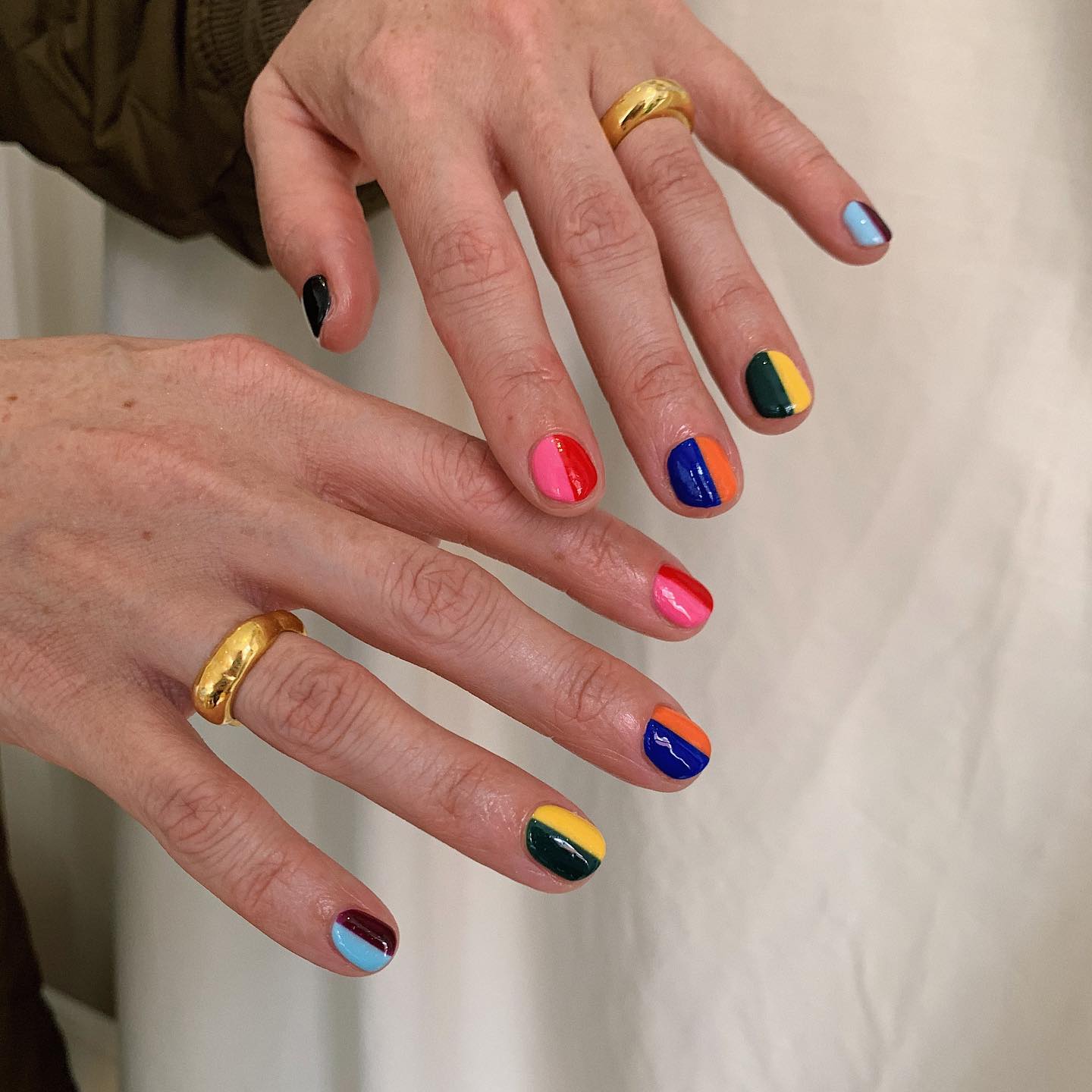 hands with gold rings in front of a white background with multicolor graphic nail polish colors