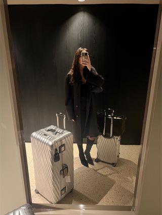 Eliza Huber posing in a mirror selfie with her two silver Tumi suitcases in Milan during Milan Fashion Week.