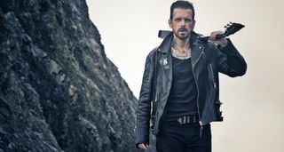 Ricky Warwick looks very Mad Max as he dresses in all black and carries a Les Paul over his shoulder in a stark landscape shot.