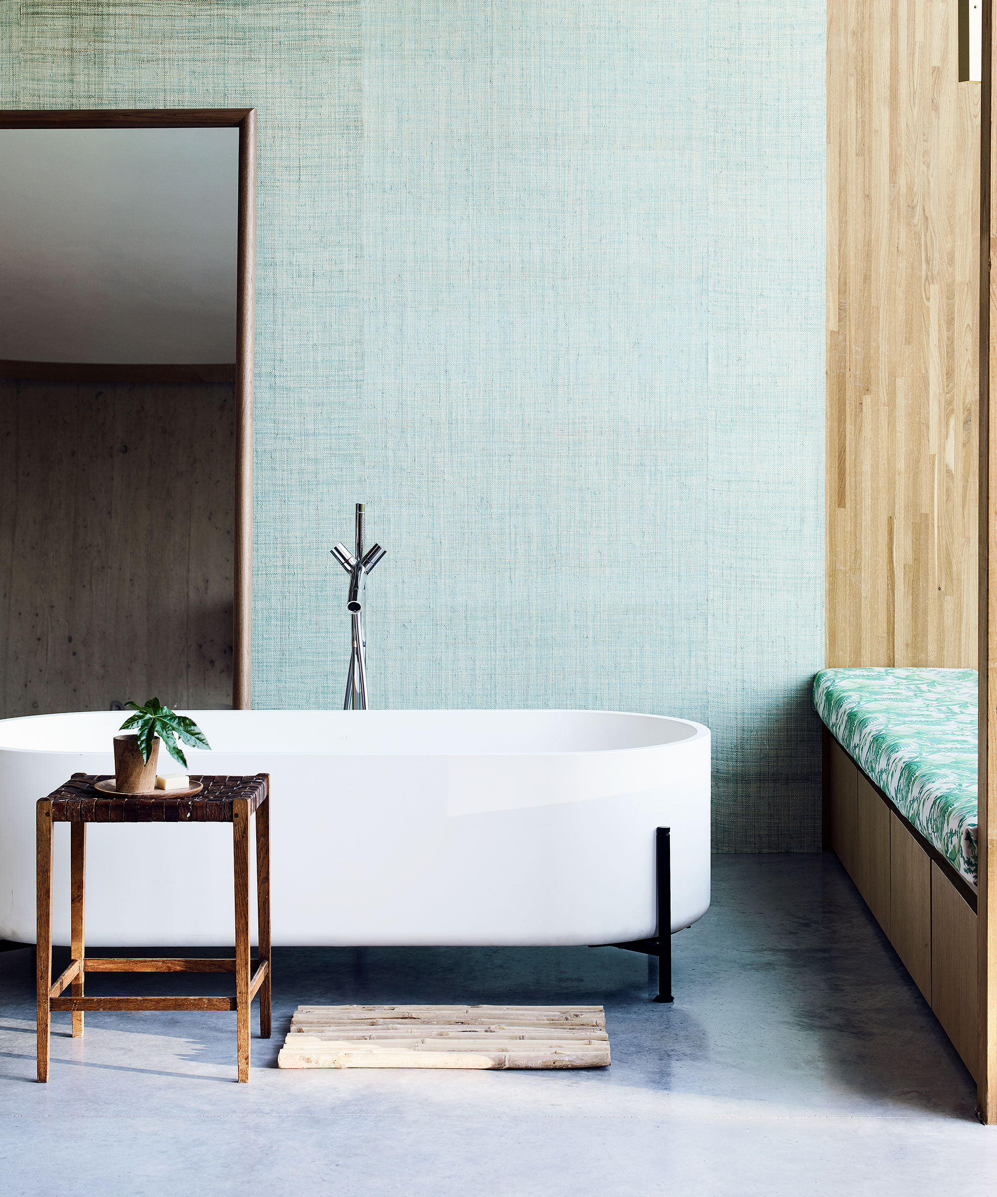 A modern white bath with black legs in front of a green wall