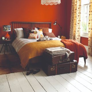 A bedroom with burnt orange-painted walls and floor boards painted in contrasting white