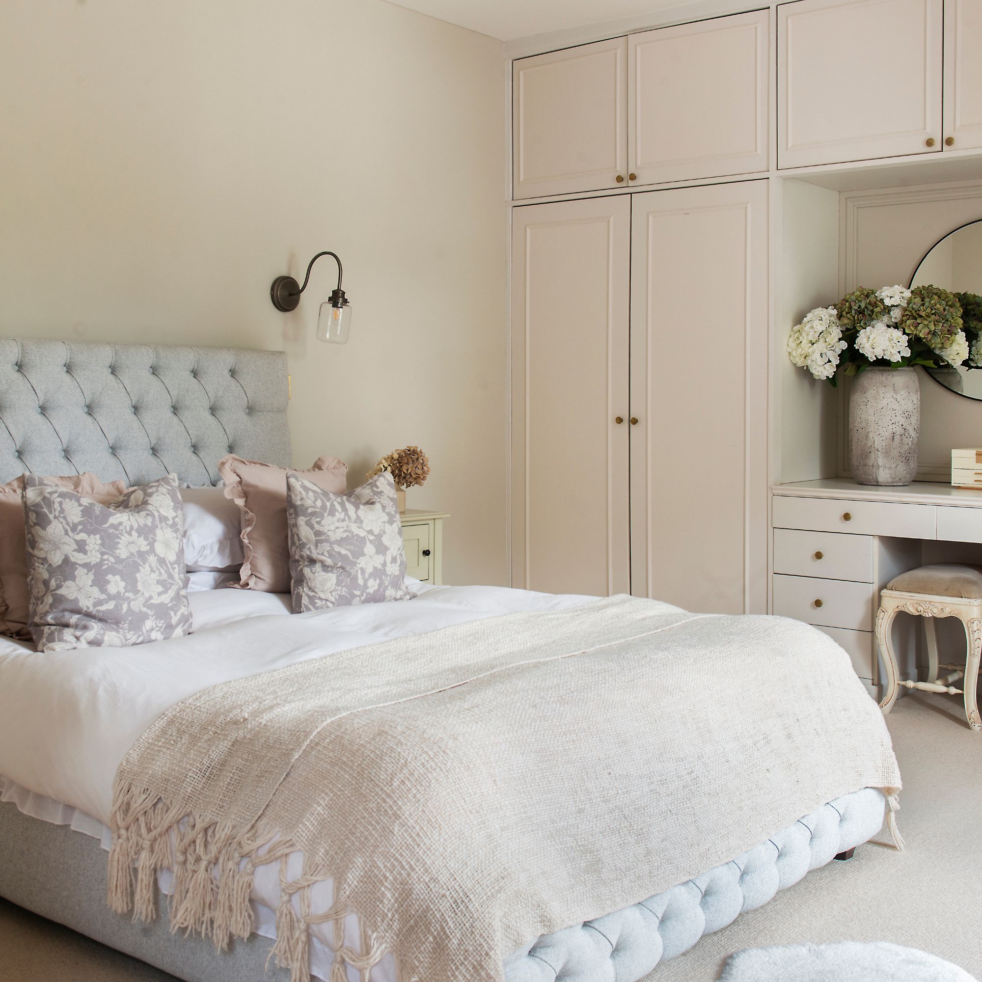 Cottage bedroom with buttoned grey bed frame, white built-in storage and wall lights