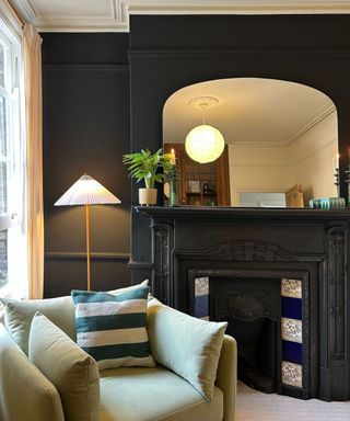 living room with black wall and fireplace, light green armchair with striped cushion, large mirror above fireplace