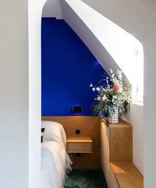 Yves Klein® Shade of blue painted on modern bedroom wall with Scandi-style wooden integrated headboard and flowers in a vase