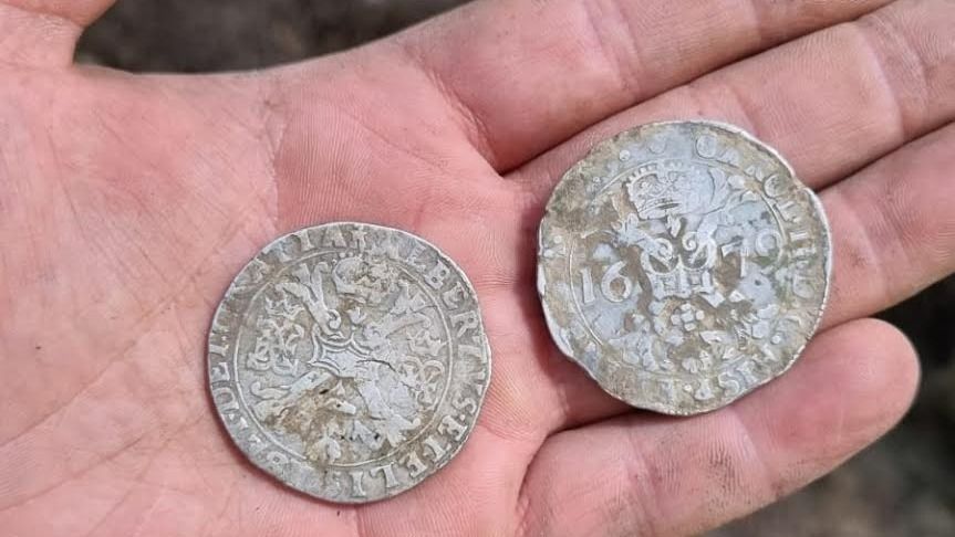 A person holds two silver coins in their hand