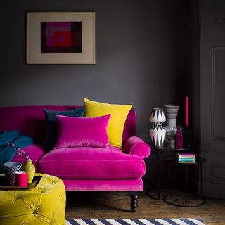 pink velvet sofa with yellow and blue cushions and throw in front of a black will with colourful artwork