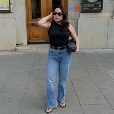 indi wears black tank, jeans, and black thong sandals while posing with a handbag