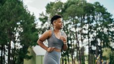 woman in a grey vest and leggings running outside with trees behind her. the shot is cropped at her hips with a side-on view.