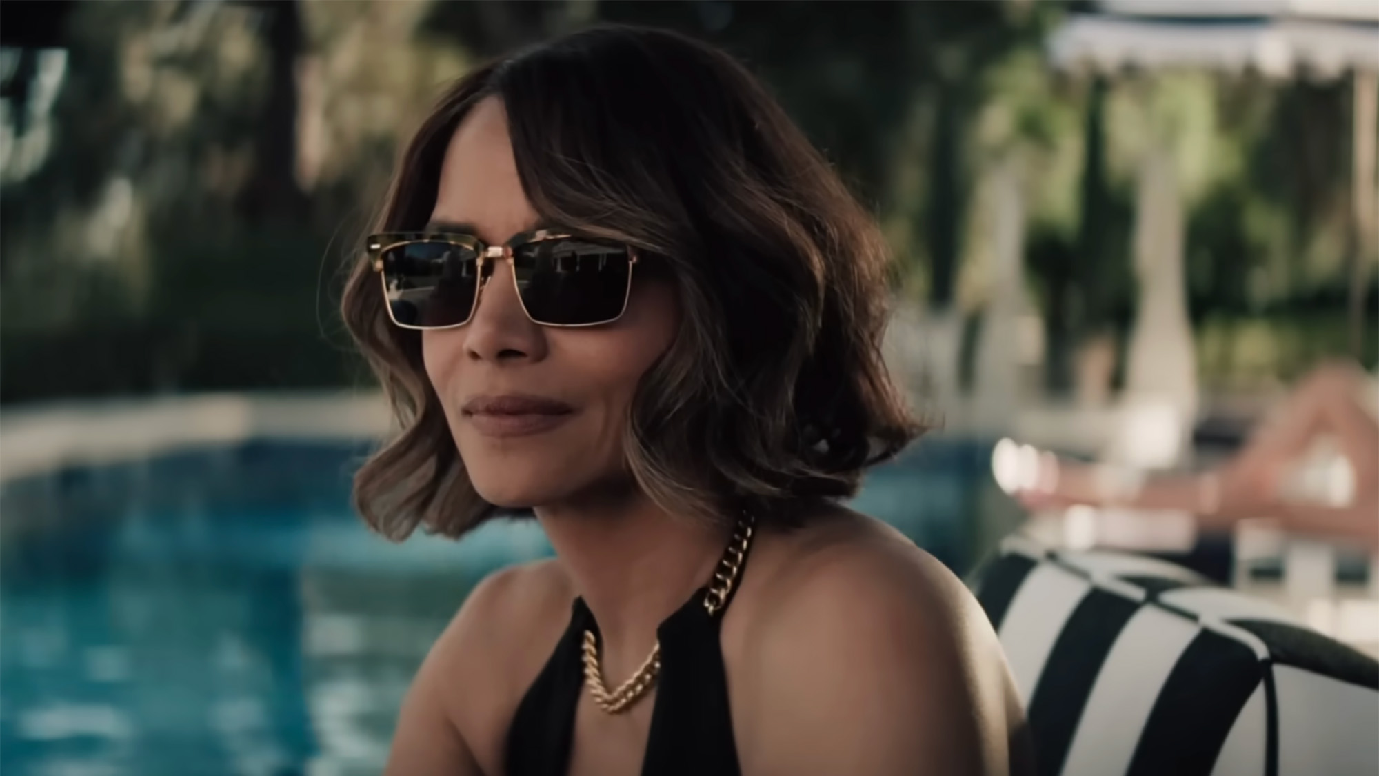 Halle Berry in a black suit and sunglasses sitting by a pool and staring into the distance in Crime 101.