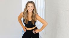 Woman in black sportswear stands with her hands on her hips and smiles at the camera
