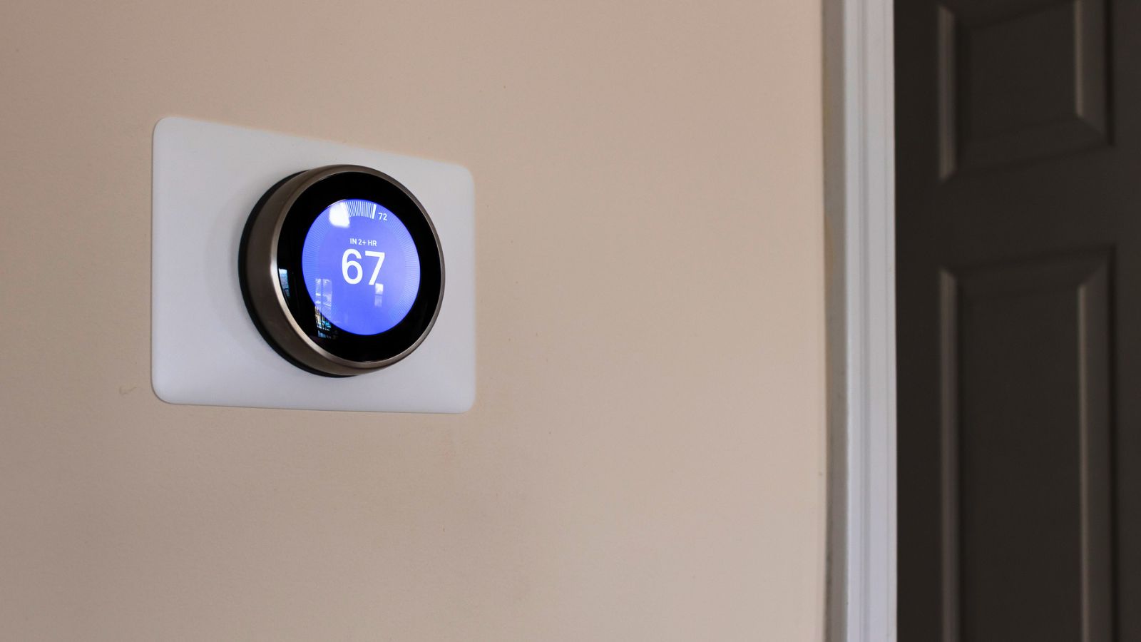 Hero shot of smart thermostat set to 67 degrees Fahrehheit on a cream wall GettyImages-1135019686