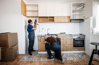 Two people installing new cabinets in a kitchen.