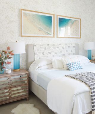 A white bedroom with beachy wall art, a white bed, and a drawer with flowers on