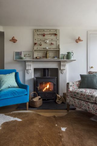 Sitting room with blue velvet armchair beside fireplace bearing distressed wooden panels and animal skin rug below