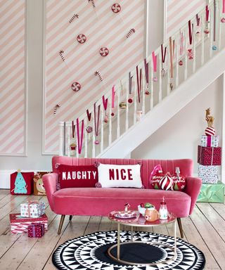 A Christmas-themed living room with pink and white striped wall decor, pink velvet sofa and baubles on banisters