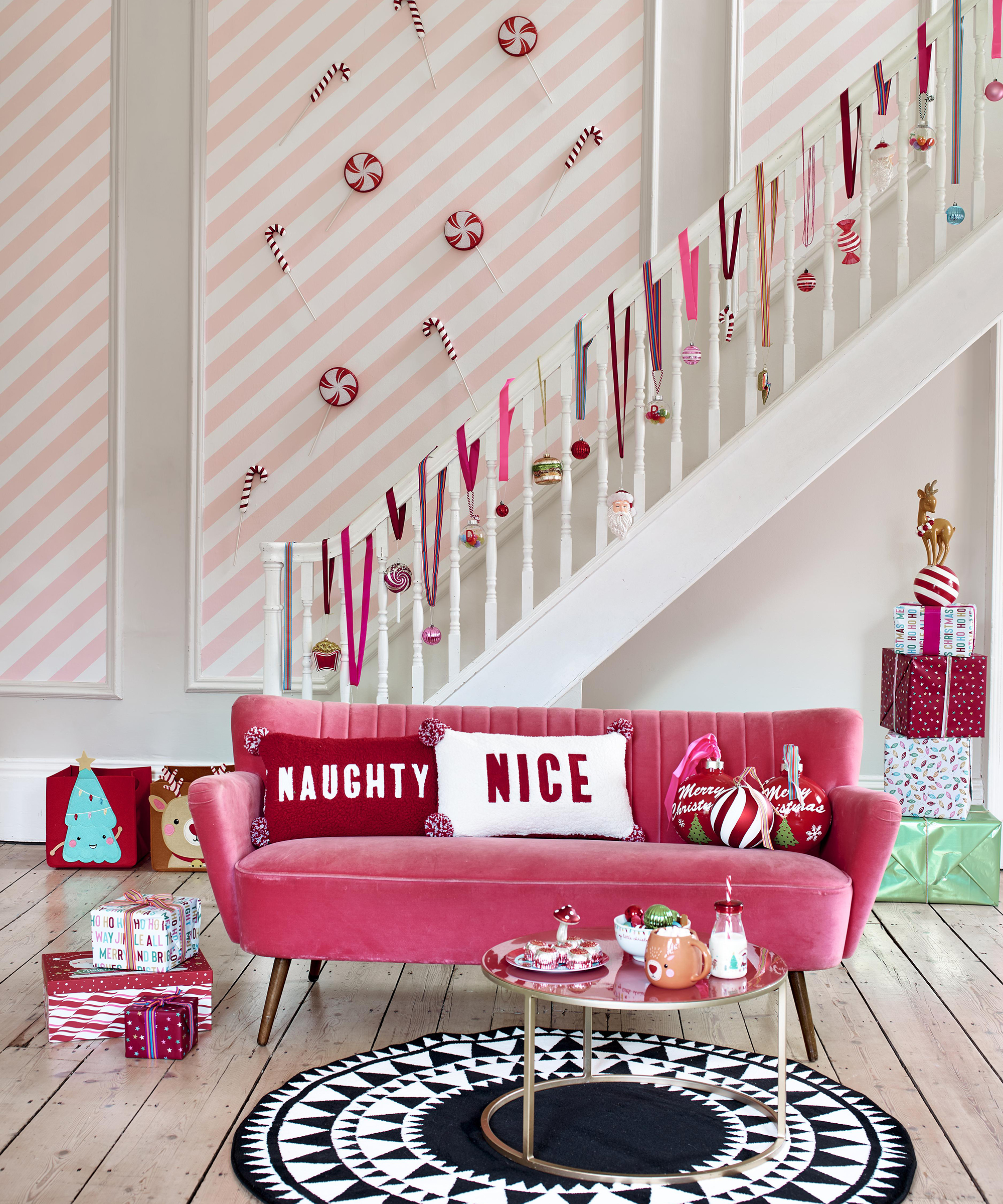 A Christmas-themed living room with pink and white striped wall decor, pink velvet sofa and baubles on banisters