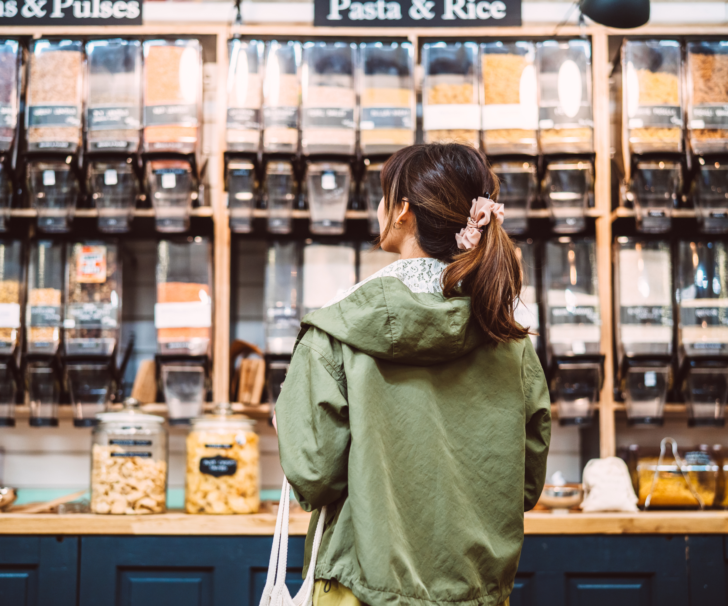 rear view of woman stood in front of dried food containers in zero waste store