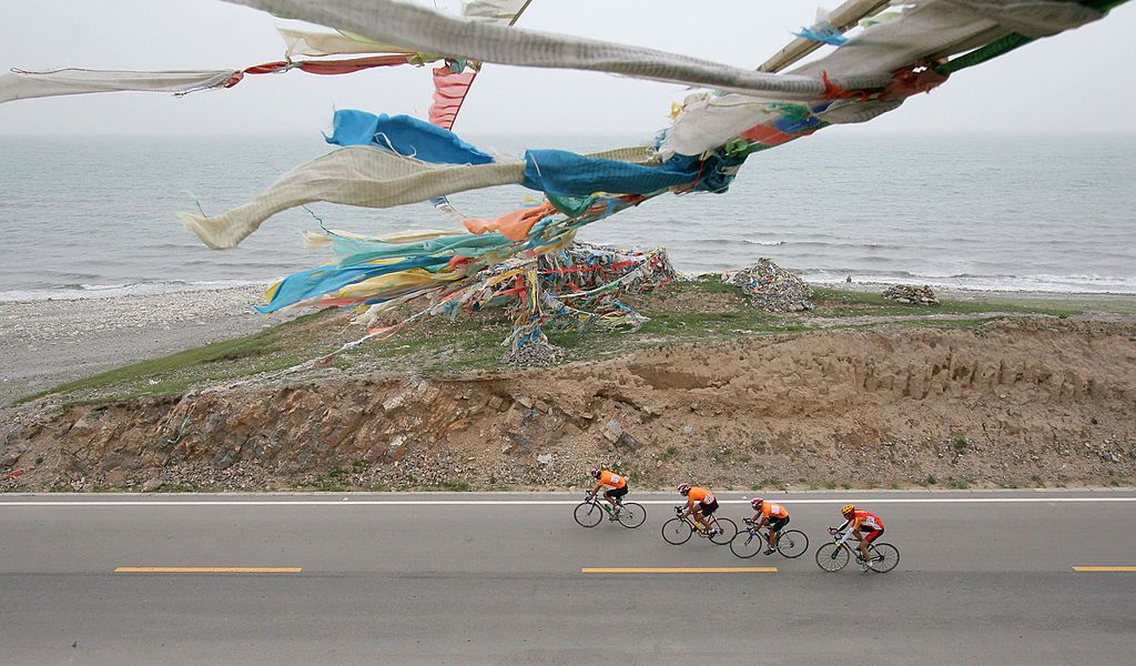 QINGHAI LAKE, CHINA - JULY 18: (CHINA OUT) Cyclists ride bicycles past Prayer Flags during the third stage of the 4th Tour de Qinghai Lake International Cycling Race along Qinghai Lake on July 18, 2005 in Qinghai Province, northwest China. The 4th Tour de Qinghai Lake will last from July 16 - 24, covering 9 stages. Twenty teams from five continents attend this year&#039;s race. Tour de Qinghai Lake is held annually since 2002. In 2004, it rose to the top road cycling race in Asia. (Photo by China Photos/Getty Images)
