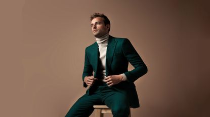 A man sitting on a stool, wearing a green suit – one of the best suits you can buy