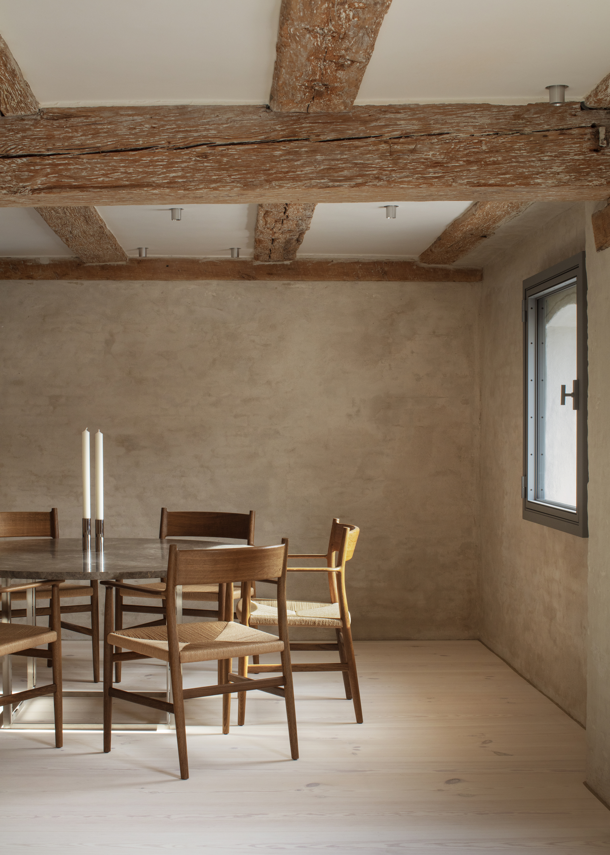 A dining room with wooden beams in the ceiling, lime washed walls, and a wooden dining table and chairs