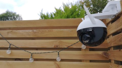 The Ezviz C8C mounted in a garden next to a wooden fence