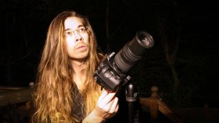 Man with long hair holding a Pentax K-1 Mark II at night