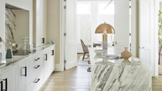 a big light-filled kitchen with a grey veined marble island and white cabinets