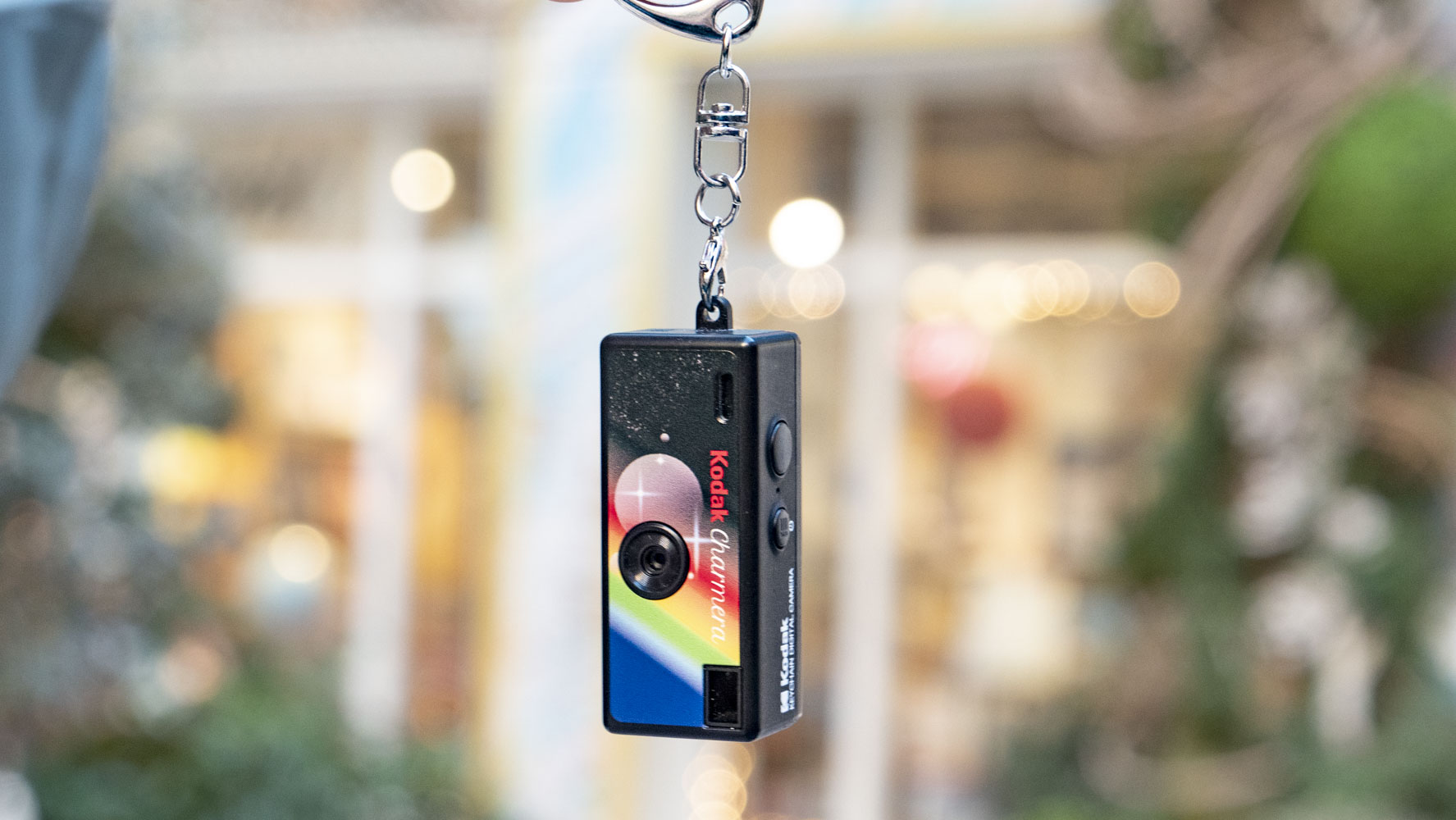 Kodak Charmera compact camera dangling from its keychain, with shop frontage backdrop