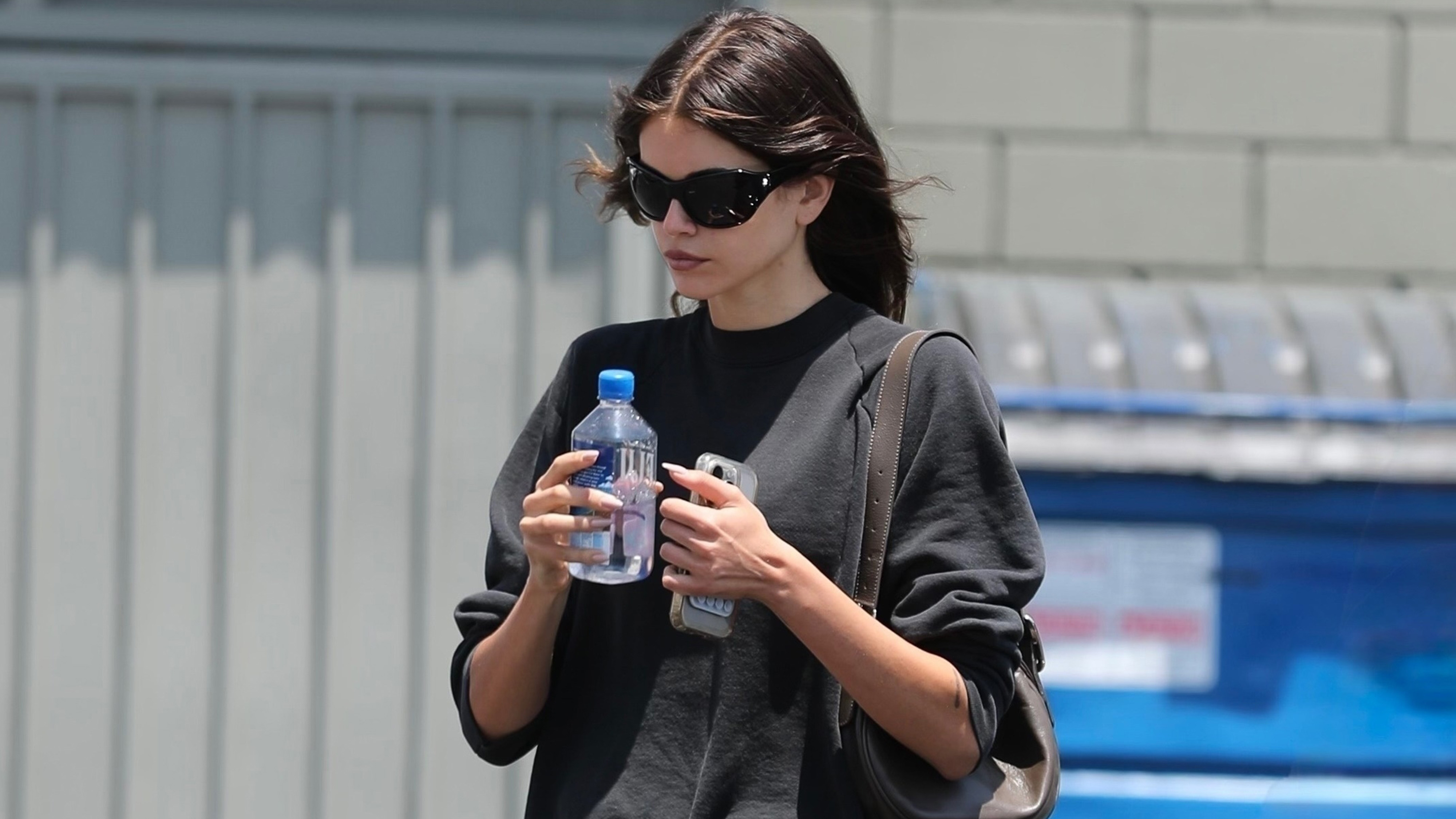 Kaia gerber wears a black sweatshirt, micro foldover shorts, and on running sneakers.
