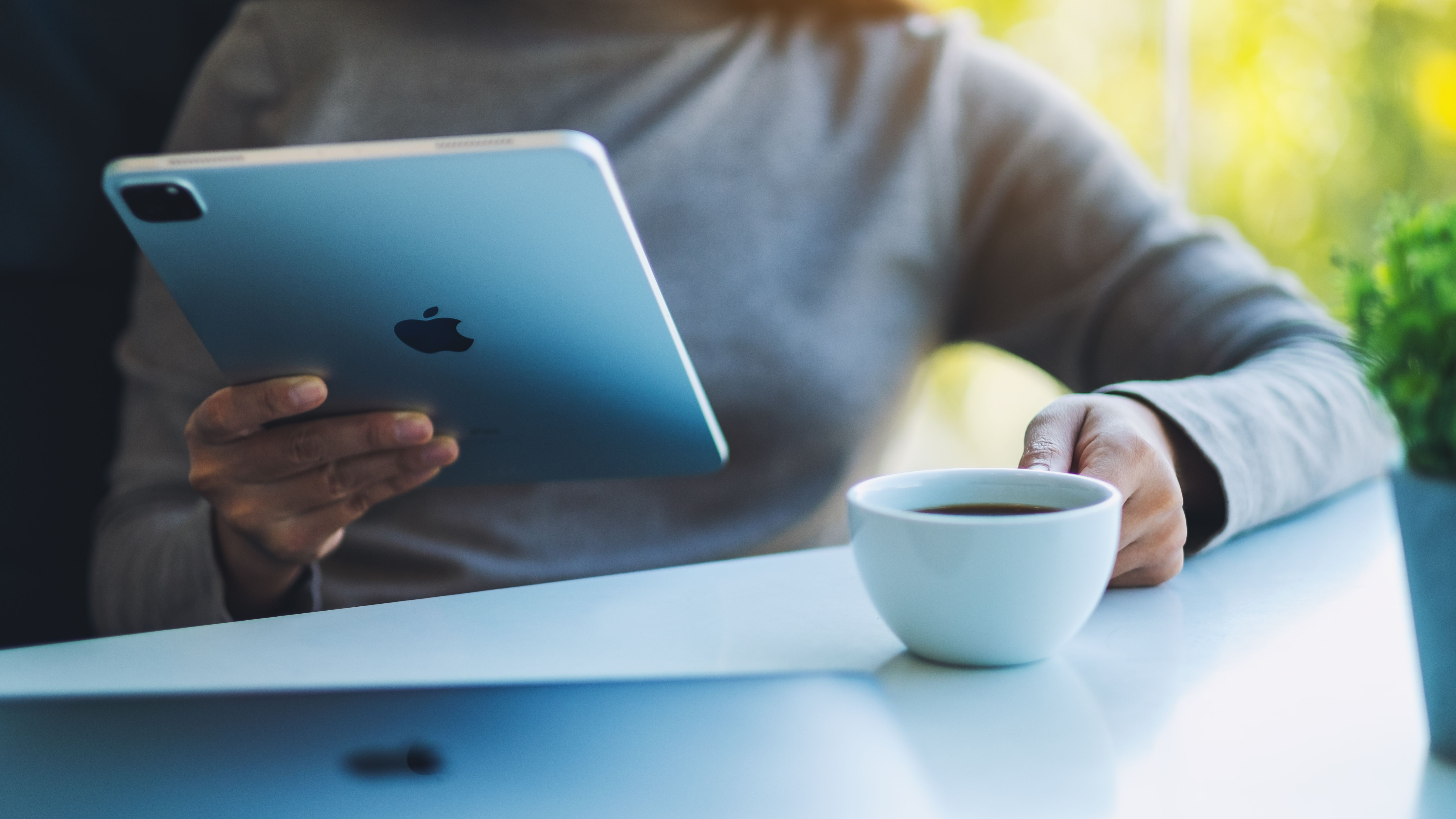 Una mujer sosteniendo y usando la tableta digital Apple New Ipad Pro 2020 con una computadora portátil Apple MacBook Pro mientras toma café