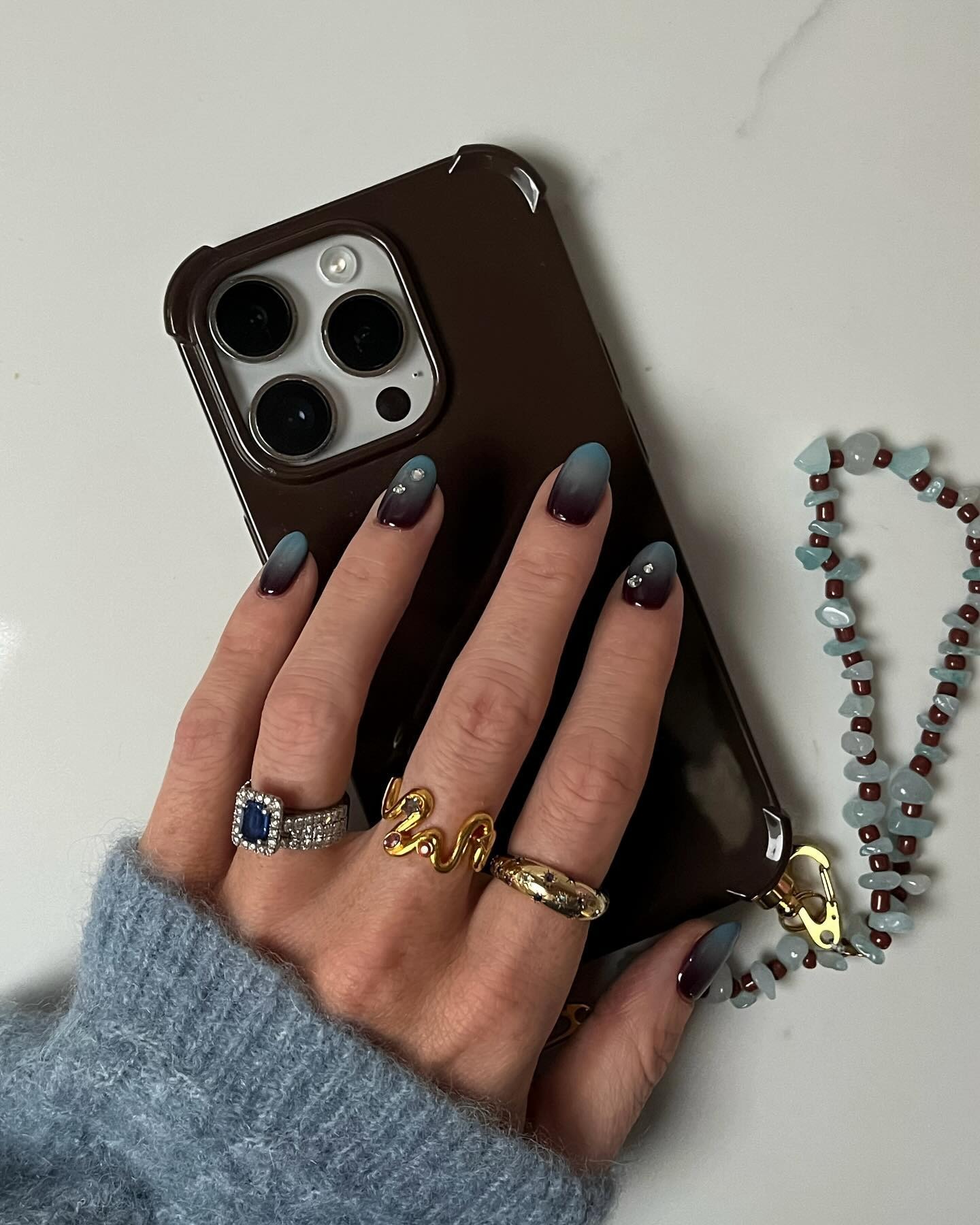 A woman with a blue and brown ombre manicure holding a brown phone case