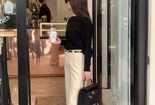 A woman wearing a black crewneck sweater with cream trousers.