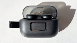 A face on view of the Specks Gemtones Play earbuds sitting in their charging case, clearly showing the press-to-release button.