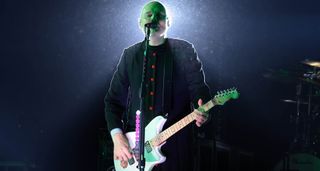Billy Corgan of the Smashing Pumpkins is haloed by a stage light and wears black as he performs live with his white signature Reverend electric guitar.