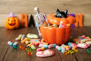 A table with a pumpkin bowl filled with sweets, with a skeleton Halloween decoration, with a scattering of sweets