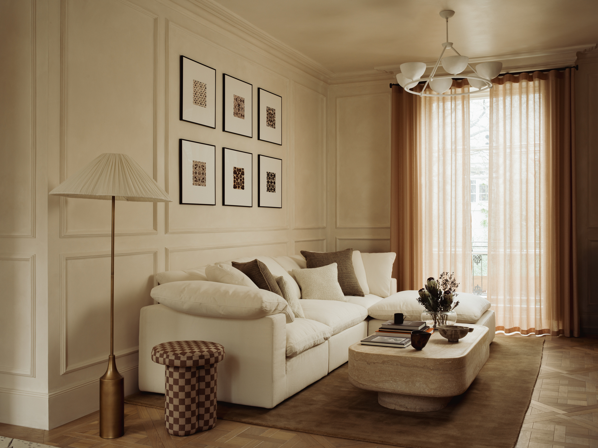 A neutral living room with wainscoting, long curtains, a white sofa, and parquet flooring