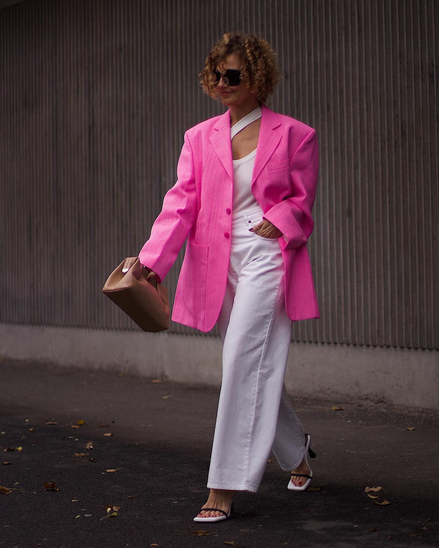 A woman wears a pink blazer, white top, white jeans, and heels.