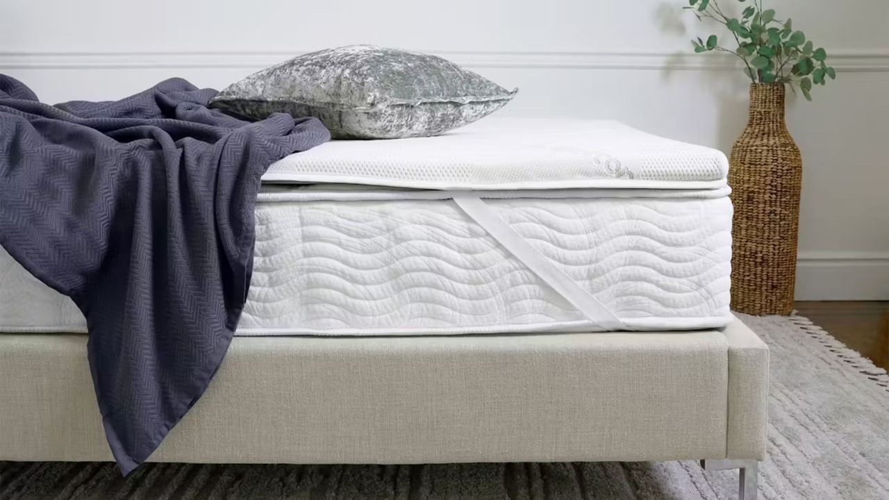 The Saatva High-Density Mattress Topper on a bed in a stylish bedroom