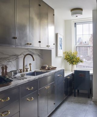 A kitchen with deep blue cabinets, brass fittings and a low window seating area