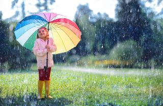 child playing in the rain with rainbow umbrella